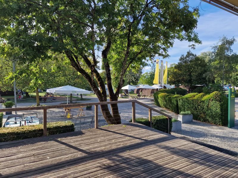 Holzterrasse am TCS Camping Genève-Vésenaz, dahinter Bäume und Wohnwagen